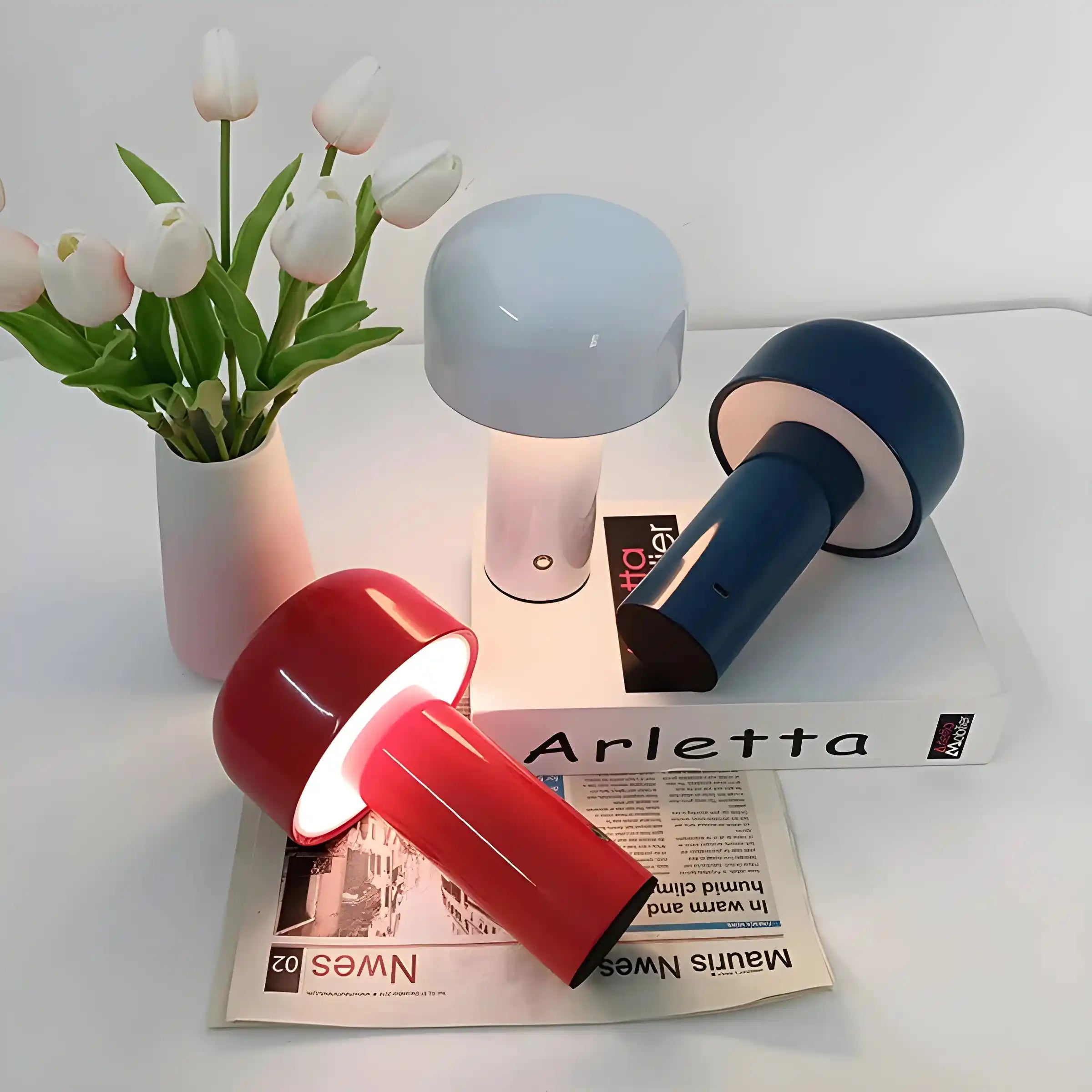 Collection of modern desk lamps in various colors alongside a vase of white tulips.