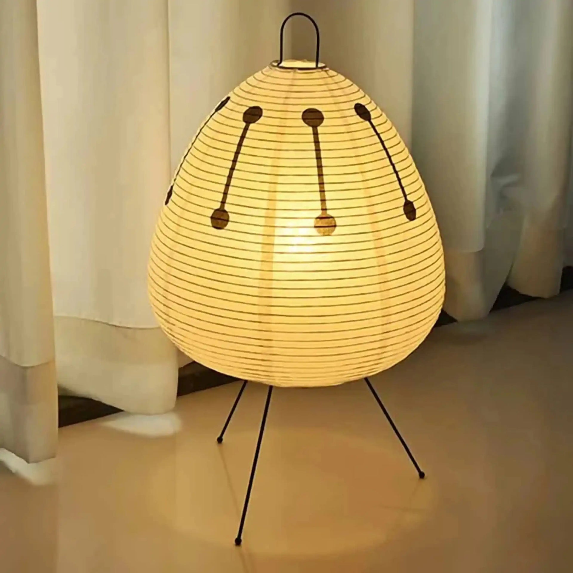 Illuminated egg-shaped paper lantern lamp on thin metal legs.