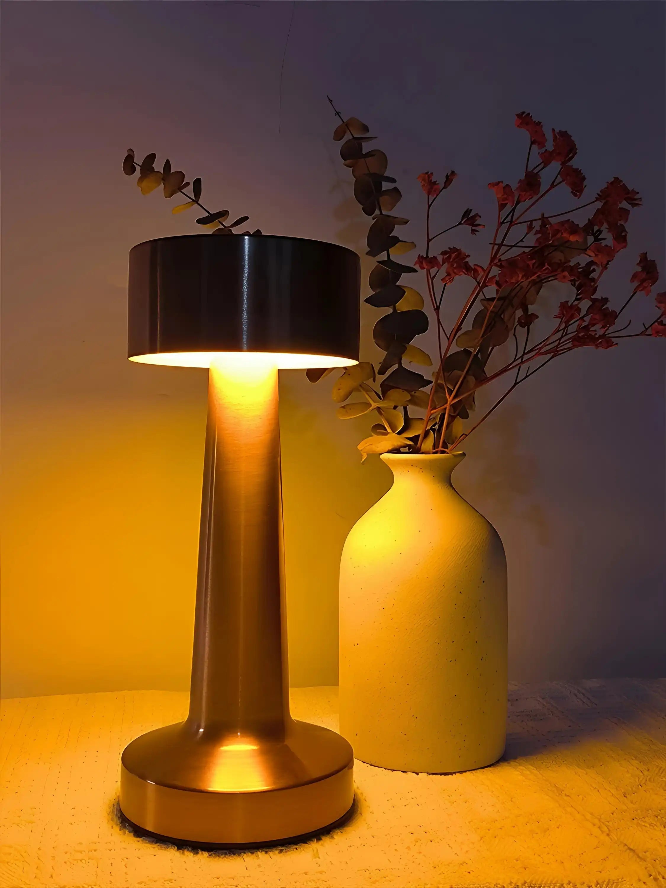 Table lamp with a cylindrical base and a black drum shade emitting warm light.